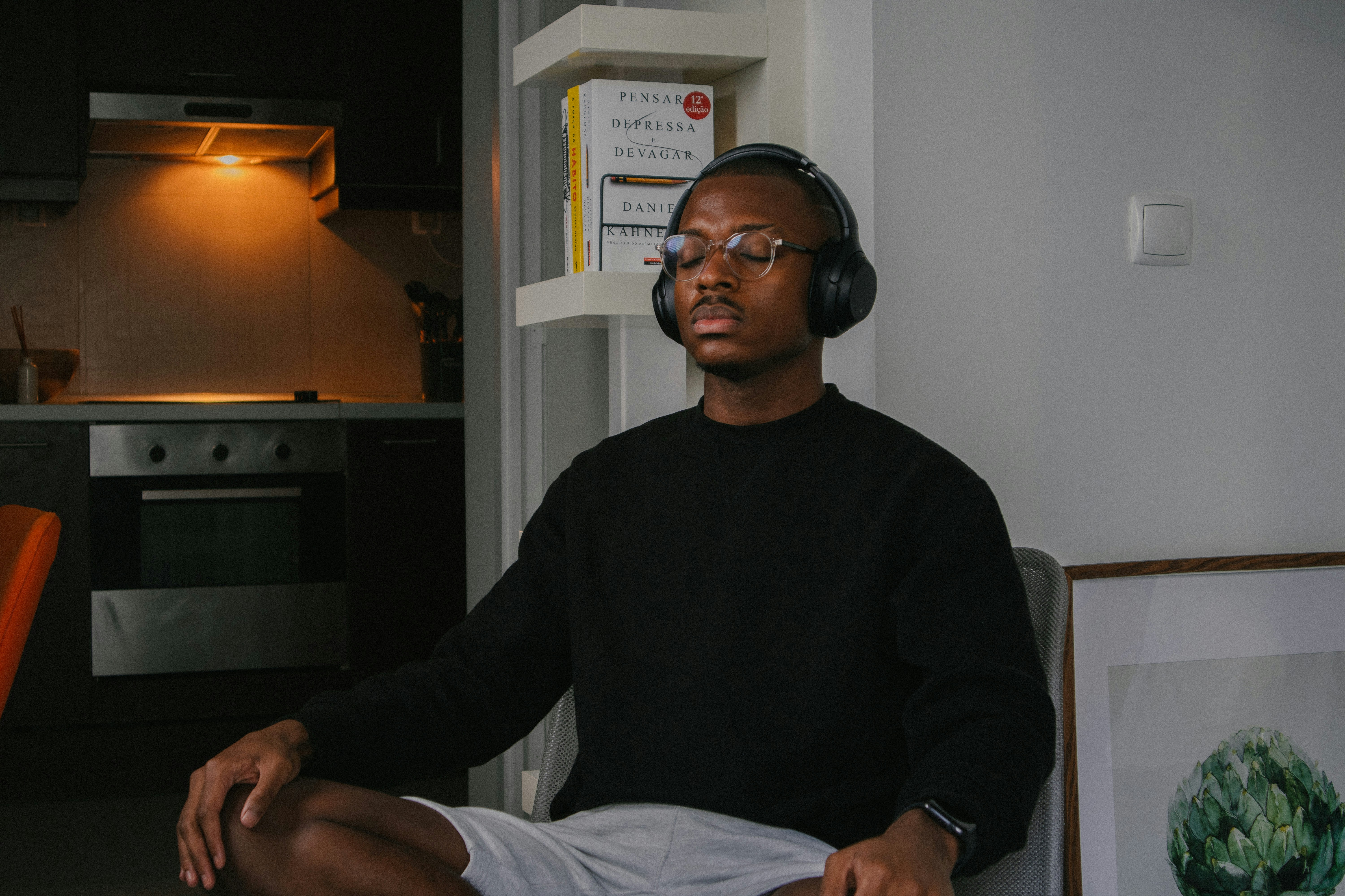 Person wearing headphones meditating peacefully with eyes closed in serene indoor setting with soft natural lighting